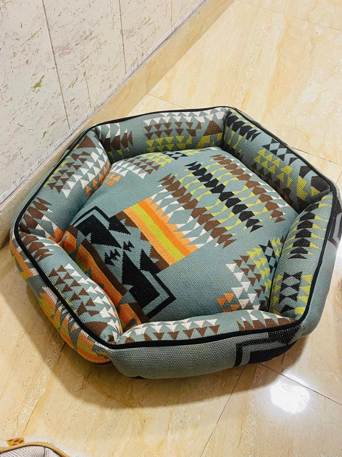 A round, padded pet bed in a grey, brown and orange Aztec-pattern knit