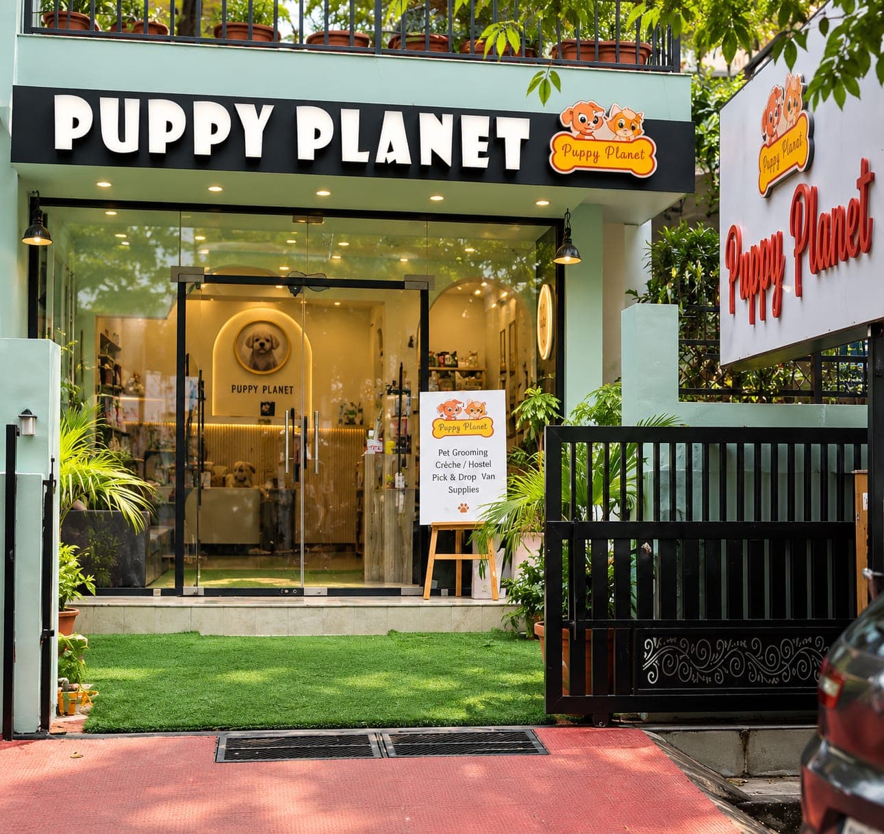 The Puppy Planet shop front: a mint-green building with a lawn, plants and a sign listing grooming, crèche and hostel, pick and drop van and supplies
