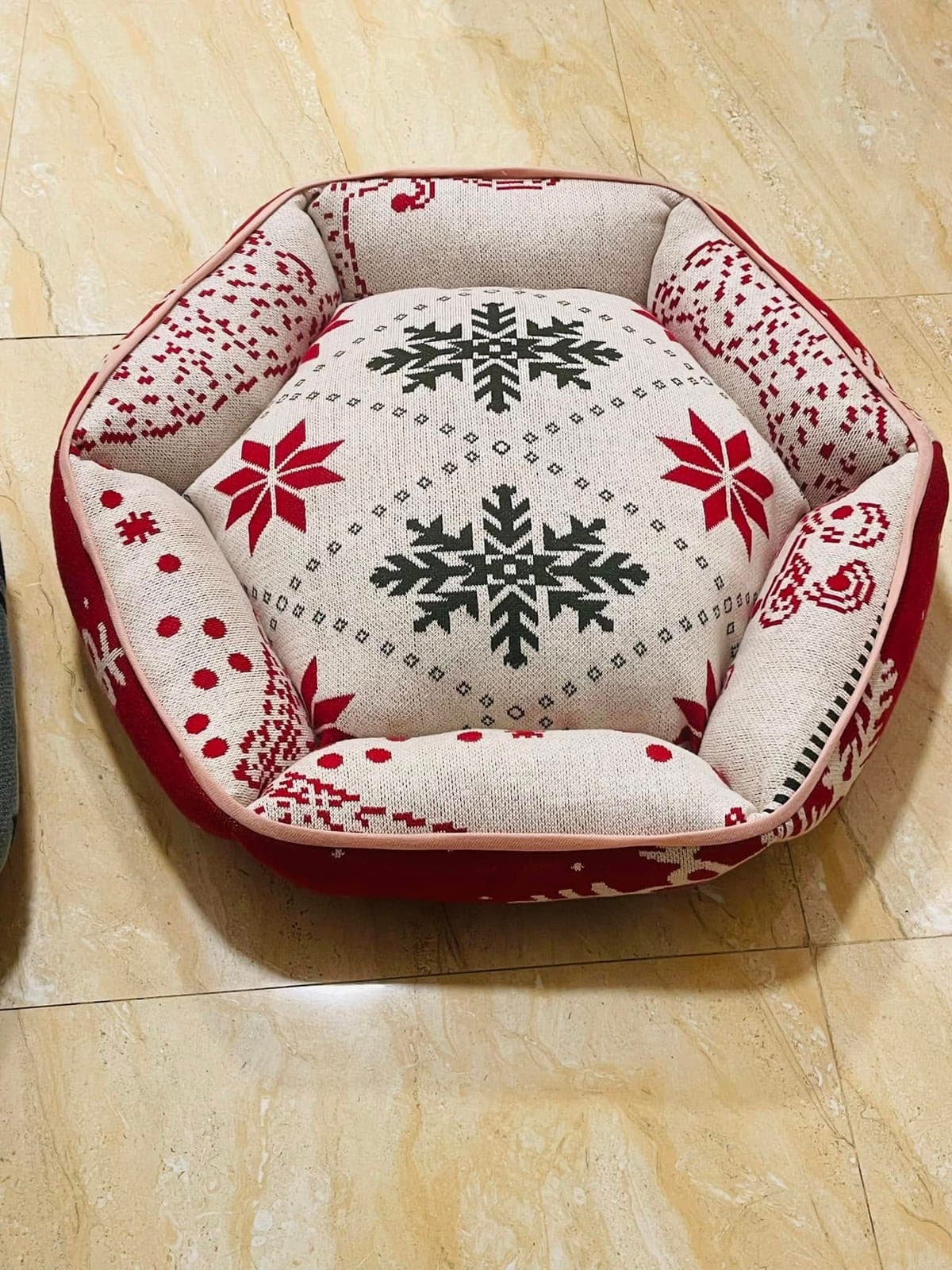 A round, padded pet bed in a red and cream snowflake knit
